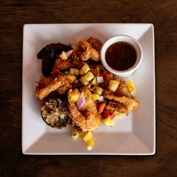 Crispy fried shrimp with pineapple salsa, grilled lemon, and a side of dipping sauce on a white plate.
