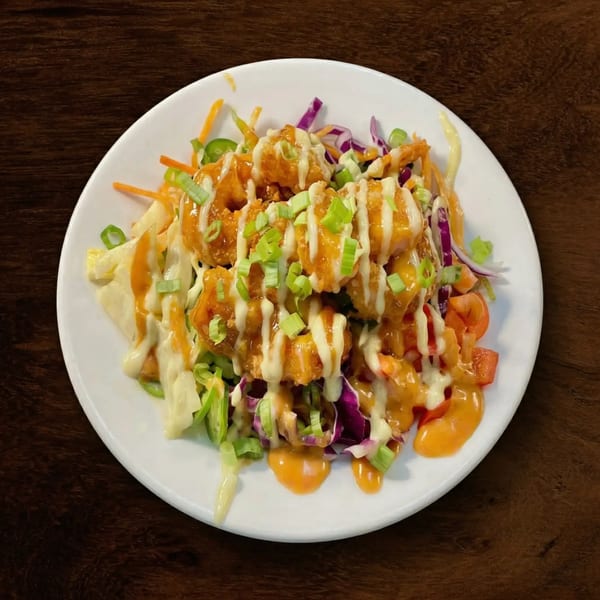 Crispy fried shrimp with orange and white sauces, green onions, and shredded vegetables on a white plate.