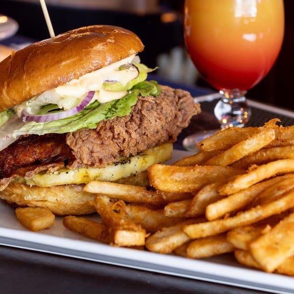 Crispy fried chicken sandwich with lettuce, red onion, and pineapple, served with fries and a drink.