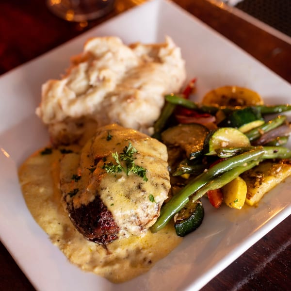 Steak with creamy sauce, mashed potatoes, and roasted vegetables on a white plate.