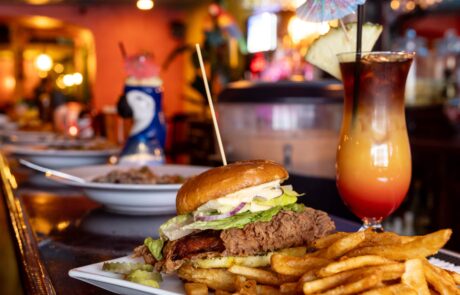 Burger, fries, and a tropical drink on the bar at the Whistling Bird